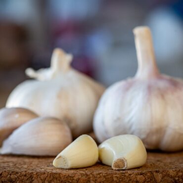 A closeup of garlic bulb and cloves on a round cork board