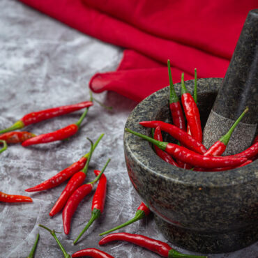 Red chillies are in a stone mortar on a black surface.