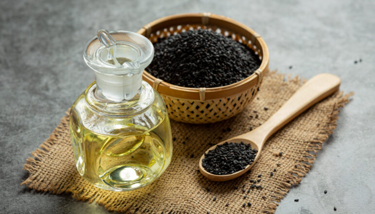 Sesame oil and raw black sesame seeds on dark background Sesame oil and raw black sesame seeds on dark background